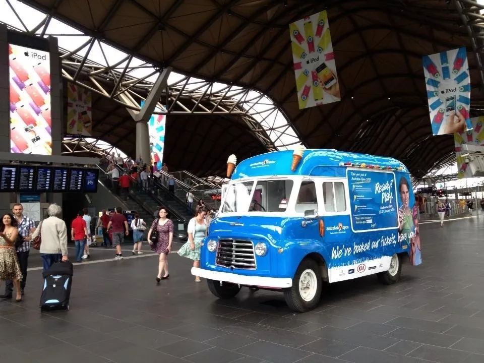 Classic ice cream van fully wrapped in blue Tennis Australia campaign branding at a railway station